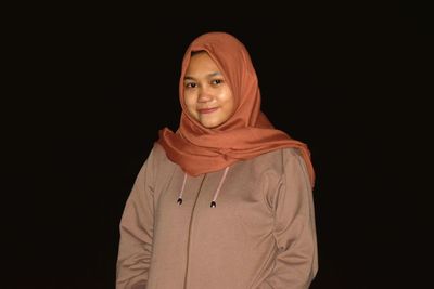 Portrait of smiling young woman against black background