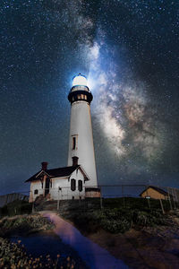 Lighthouse by building against sky at night