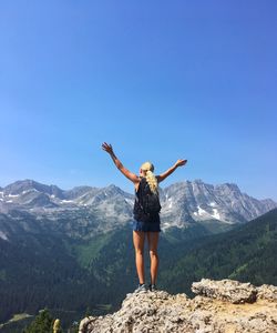 Rear view of young woman standing on mountain against clear blue sky