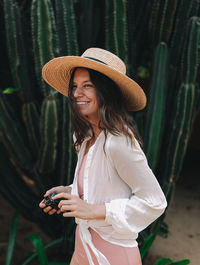 Smiling woman wearing hat while walking by plants