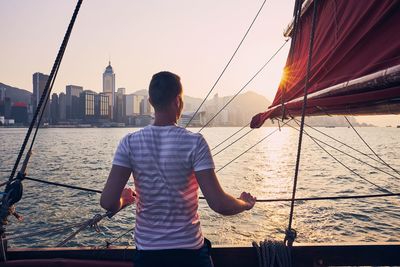 Rear view of man on sailboat sailing at bay against sky