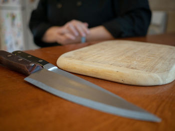 Midsection of person with cutting board and knives on table