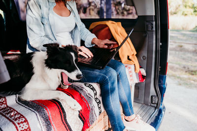 Midsection of woman using laptop while sitting with dog in camper trailer