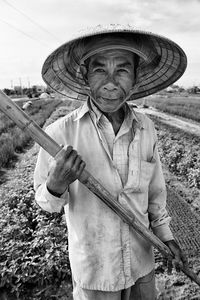 Close-up portrait of man holding bamboo standing on agricultural field against sky