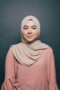 Portrait of smiling young woman wearing hijab against gray background