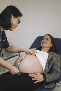 Smiling doctor measuring abdomen of pregnant patient lying on examination table in medical clinic