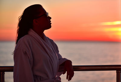 Woman looking at sea against sky during sunset