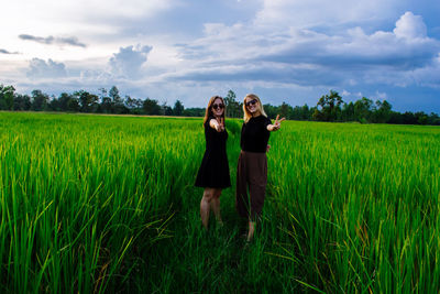 Portrait of smiling women embracing while standing on field against sky