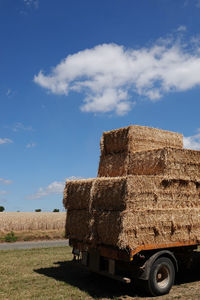 Stack of hay bales on field against sky