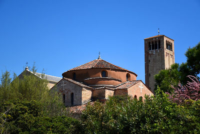 Low angle view of trees and building against clear blue sky