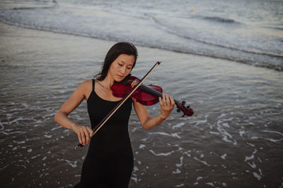 Woman playing violin in front of sea at beach