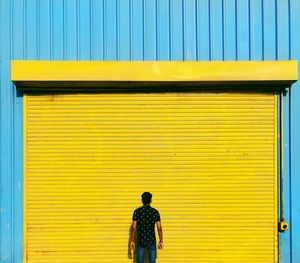 Rear view of man standing against closed yellow shutter