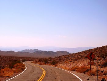 Road leading towards mountains against clear sky