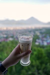 Midsection of person holding drink against mountain