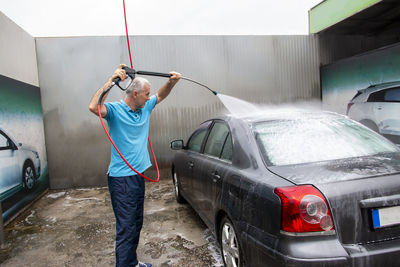 Mature man cleans automobile with covered with foam shampoo chemical detergent carwash self service