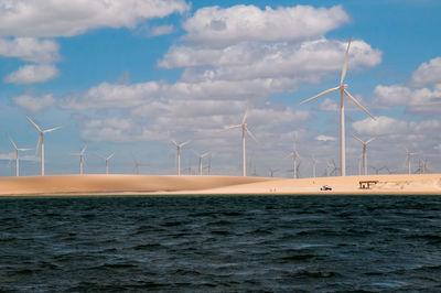 Wind turbines by sea against sky