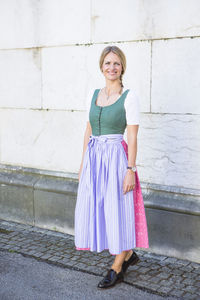 Portrait of smiling woman standing on street against wall