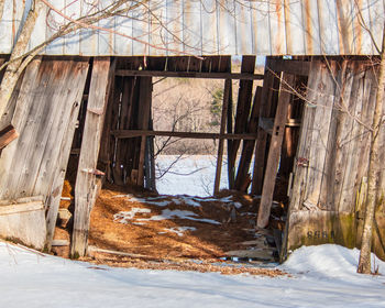 Abandoned house by bare trees on snow covered field against building