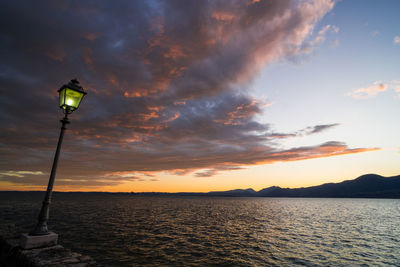 Street light by sea against sky during sunset