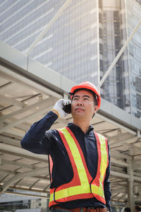 Architect talking on mobile phone while standing against buildings in city