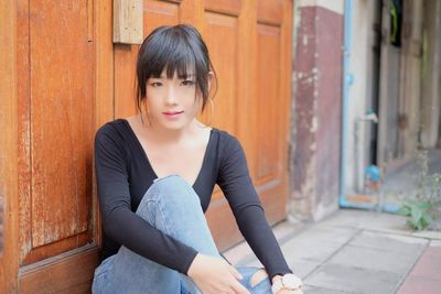 Portrait of beautiful young woman sitting outside closed house