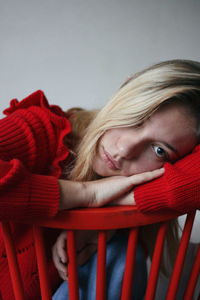 Close-up portrait of sad young woman leaning on red chair