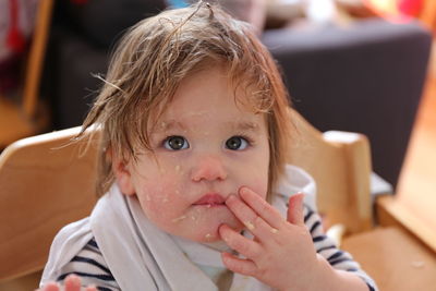 Close-up of cute baby girl with messy face looking away while sitting on chair at home