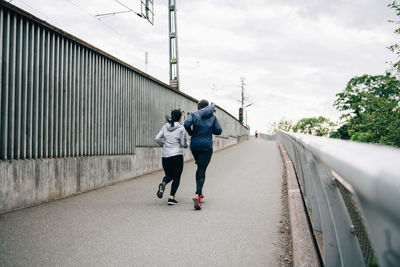 Rear view of male and female athlete jogging on footbridge in city