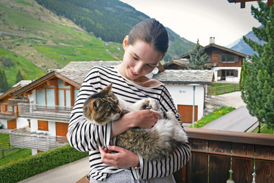 Smiling woman holding cat while standing at balcony 