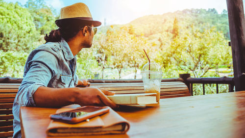 Side view of young man looking away while sitting on table