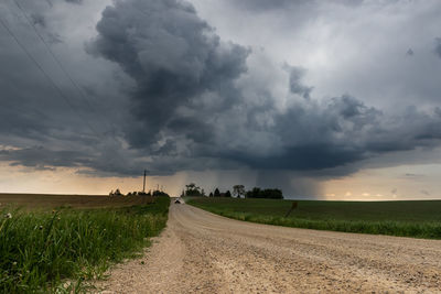 Dirt road amidst field against sky