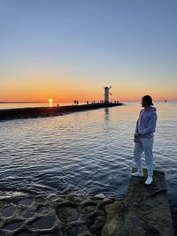 Man standing on sea against sky during sunset