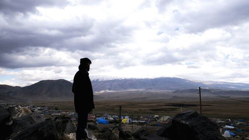 Side view of silhouette man standing on field against cloudy sky