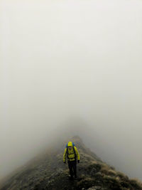 Rear view of man standing on mountain during foggy weather