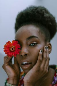 Close-up portrait of young woman holding red flower at home