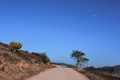 Road amidst desert against clear blue sky