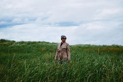 Woman looking away while standing on field against cloudy sky