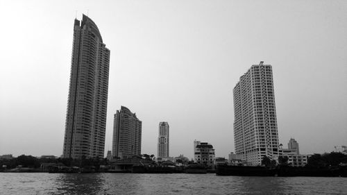 Modern buildings by river against sky in city