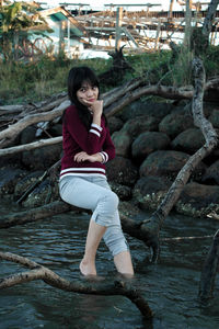 Smiling young girl looking away while sitting on fallen tree over river