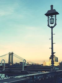 Suspension bridge in city against sky during sunset