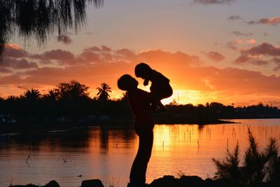 Silhouette of father playing with son by lake