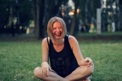 Portrait of smiling woman sitting on field against trees