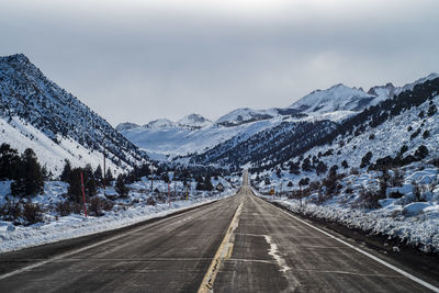 Road leading towards snowcapped mountains against sky