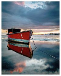 Boat moored on beach against sky during sunset