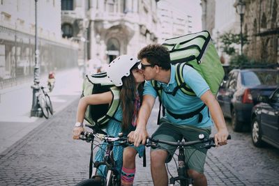 Couple kissing while riding bicycles on street in city