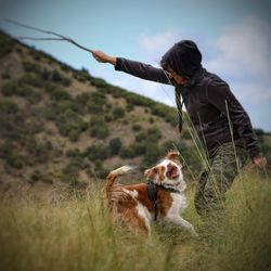 Man playing with dog on grassy field against sky