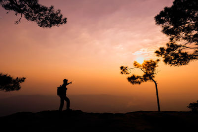 Silhouette man photographing against sky during sunset