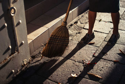 Low section of woman brooming footpath during sunny day