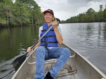 Man rowing while sitting in boat against lake