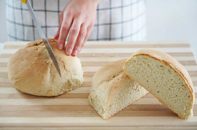 Woman cutting homemade bread on wooden table at home